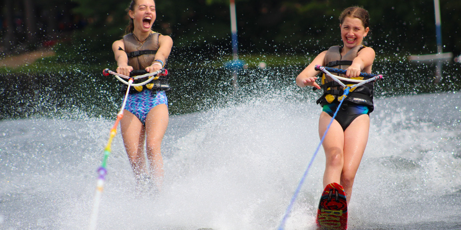 Two girls waterski and laugh in tandem at camp.