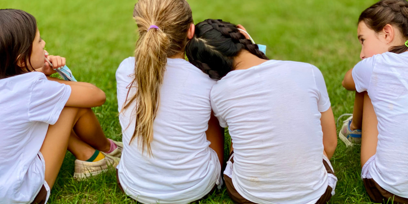 Girls in white shirts sit together with backs facing the camera.