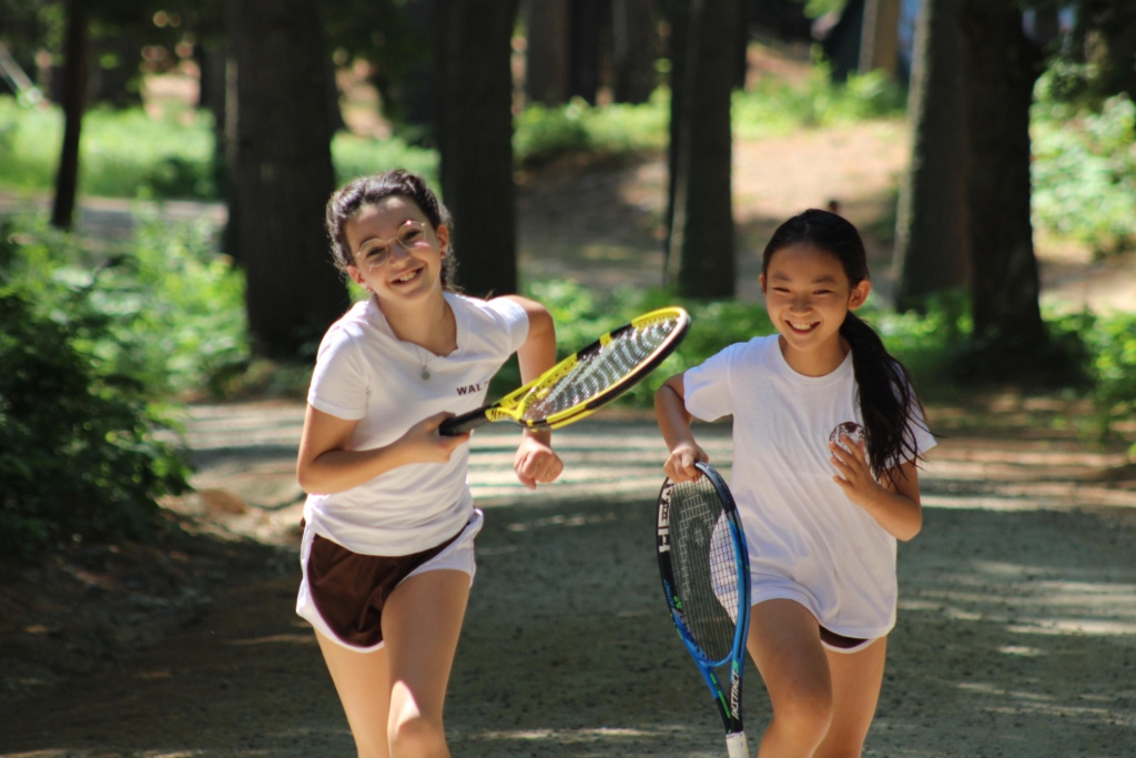 Two campers running with their tennis rackets.