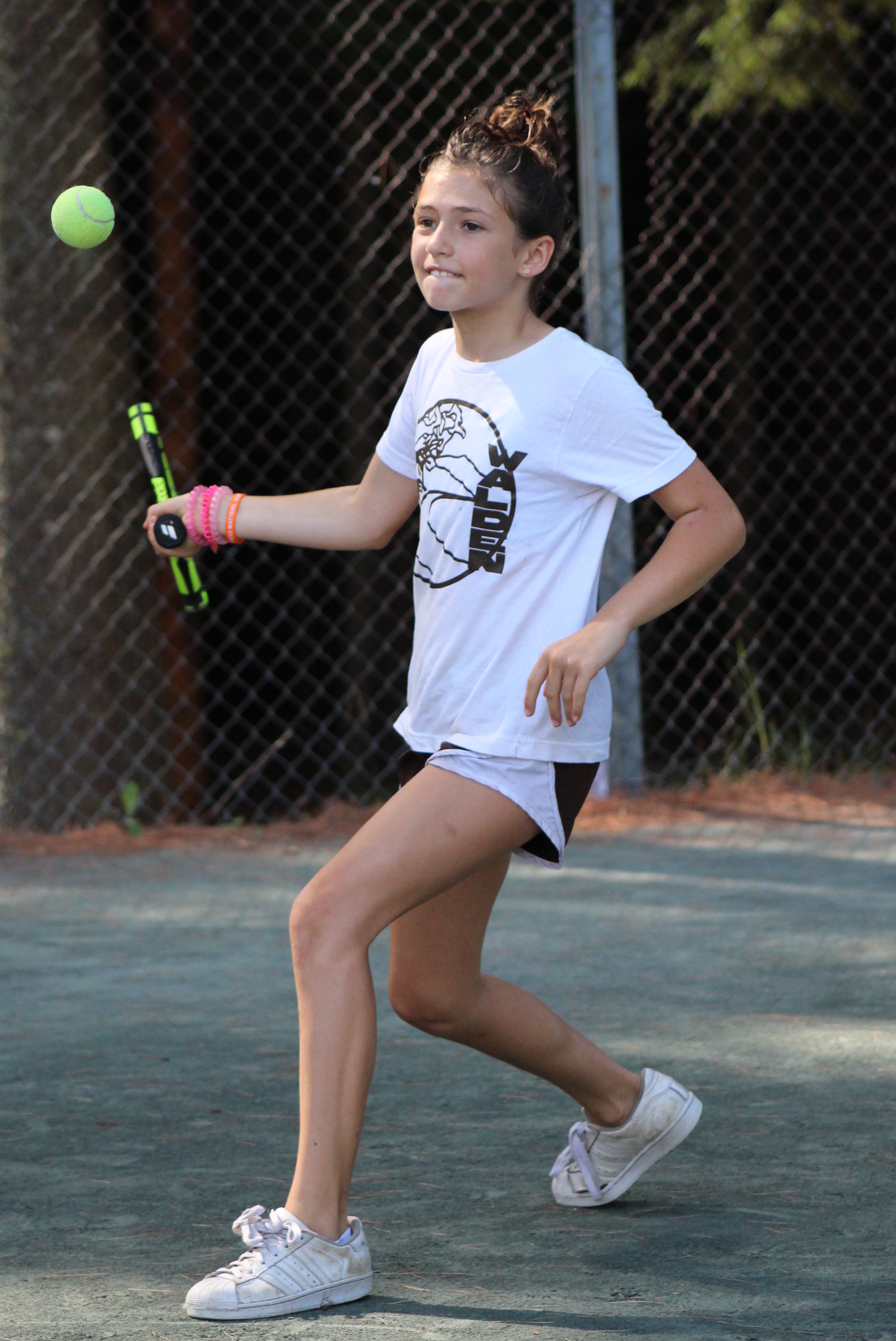 A young camper swings a forehand stroke while playing tennis. 
