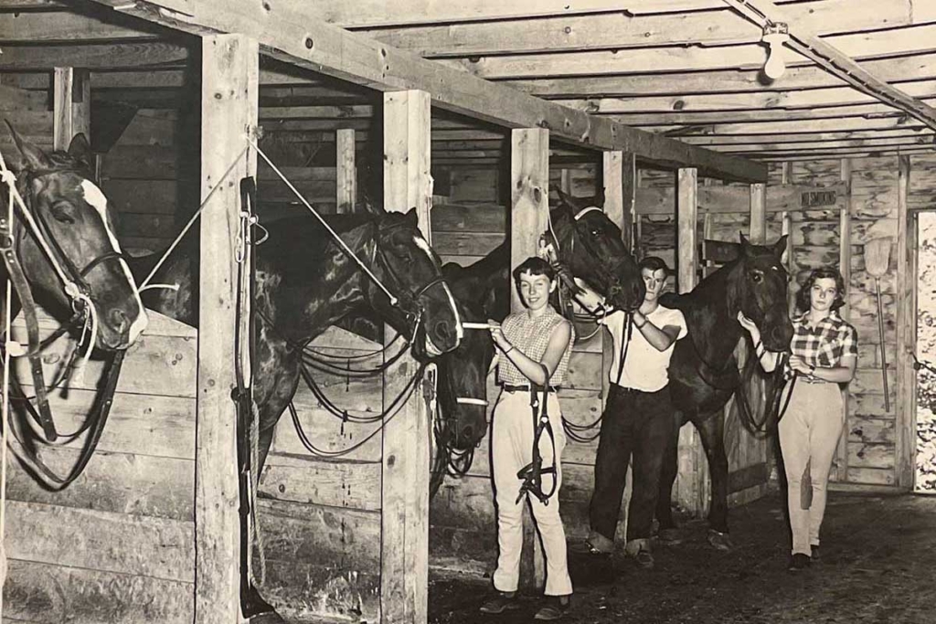 Historic scene from Camp Walden of campers working with horses in the equestrian barn.