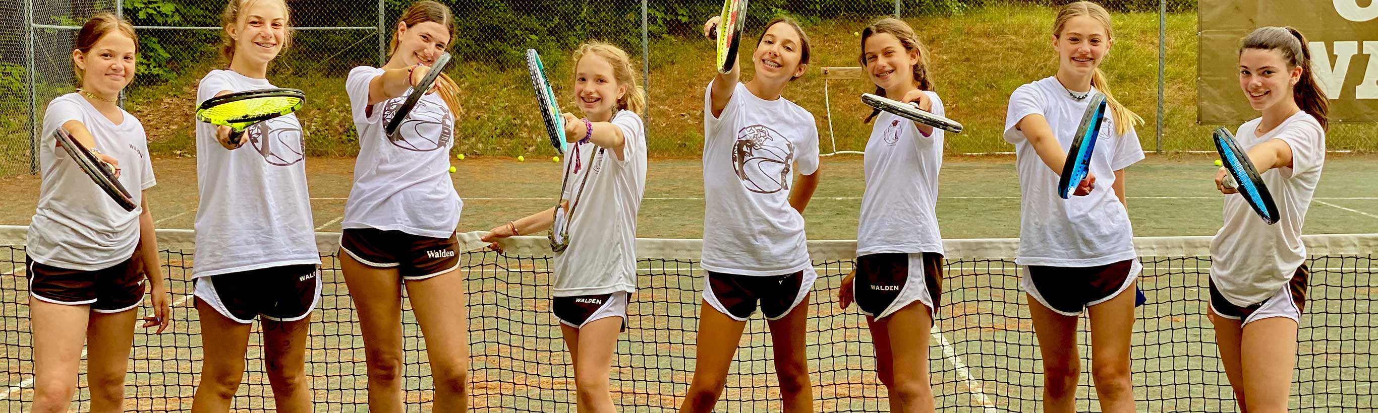 A group of girls on the tennis court pose with their rackets.