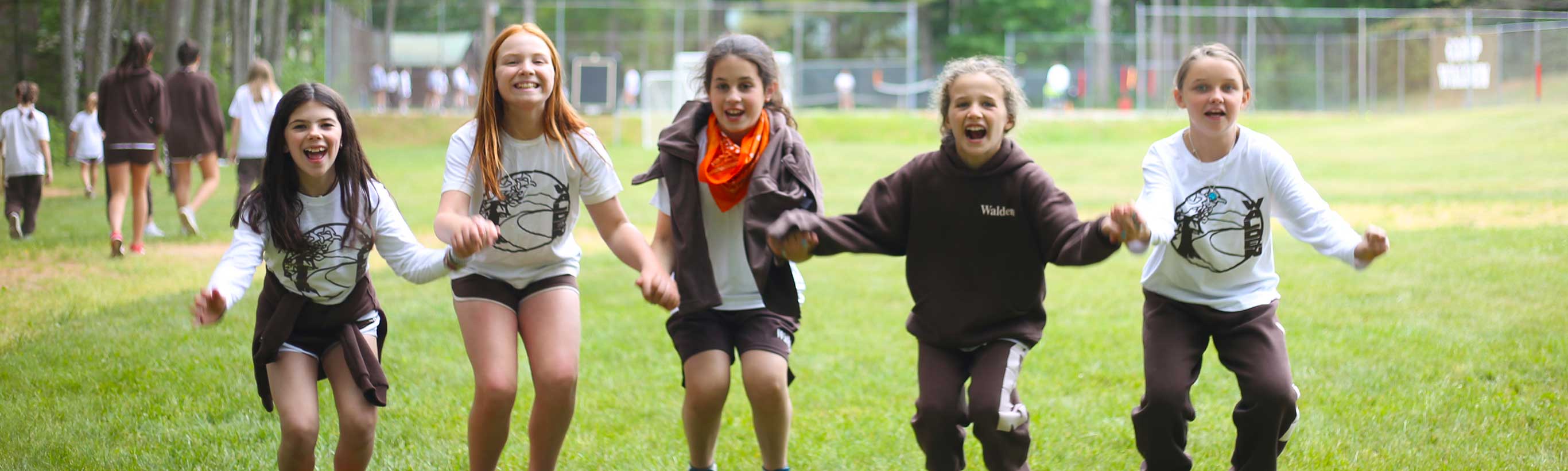 Young girls hold hands and jump in excitement at camp.