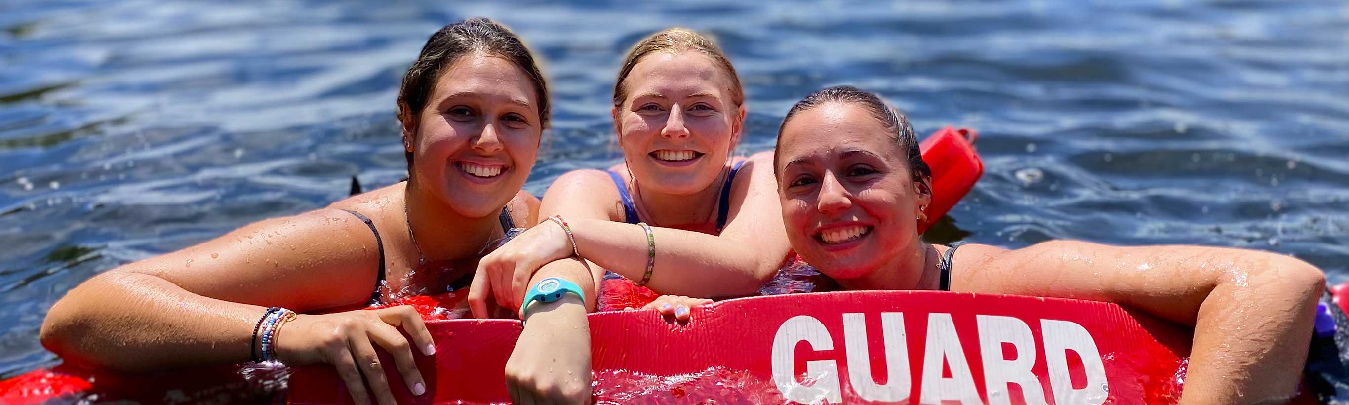 Three female camp counselors swim together with their Life Guard floatations.